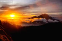 booking pendakian sunrise — Pemandangan matahari terbit yang memukau dari puncak Gunung Batur dengan latar belakang Danau Batur di Bali.