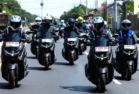 hemat BBM Yamaha NMAX — Sepeda motor Yamaha NMAX berwarna hitam sedang melaju di jalan raya perkotaan.