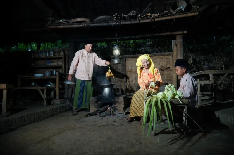 Seorang lansia sedang berdiskusi dengan anggota keluarganya di ruang tamu rumah.
