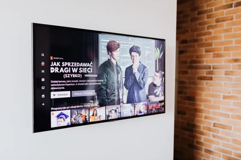 Logo JustWatch TV pada layar televisi pintar dengan latar belakang antarmuka aplikasi streaming.
